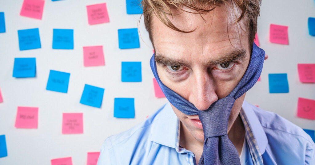 A imagem ilustra um empresário estressado e decepcionado. Ao fundo, um quadro branco com diversos post its.